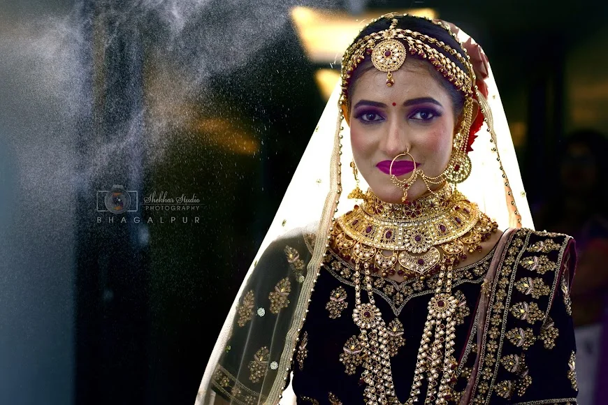A bride in black and gold wearing ornate jewellery with a light veil behind her