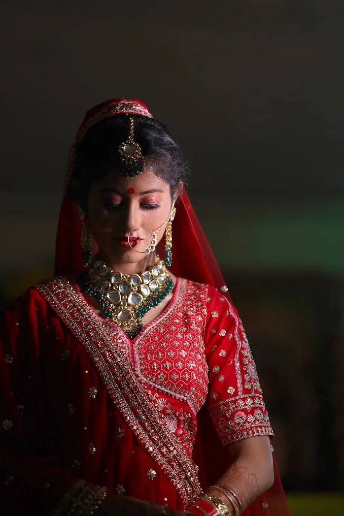 A bride in red looking down in soft directional light against a dark background