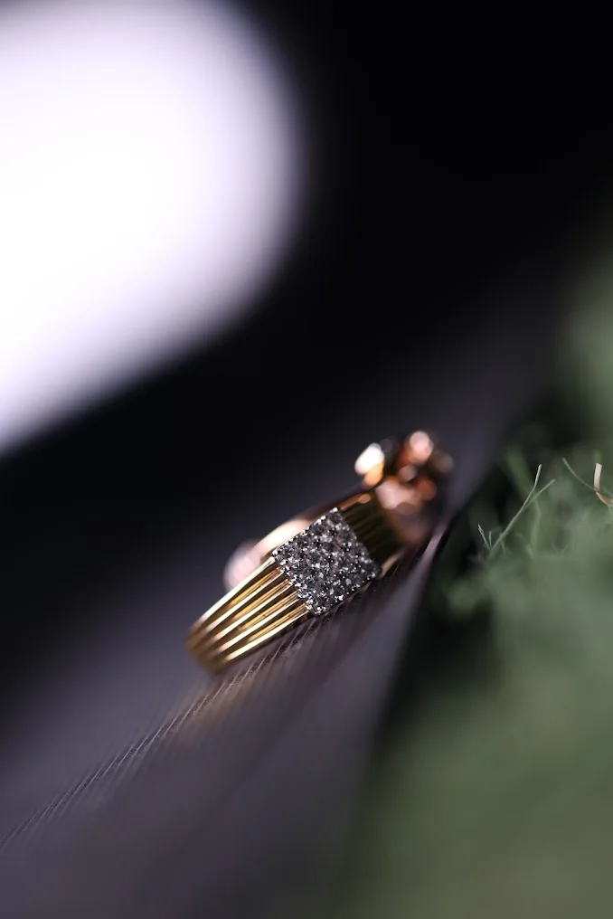 A gold ring photographed vertically on a dark surface with soft reflected light