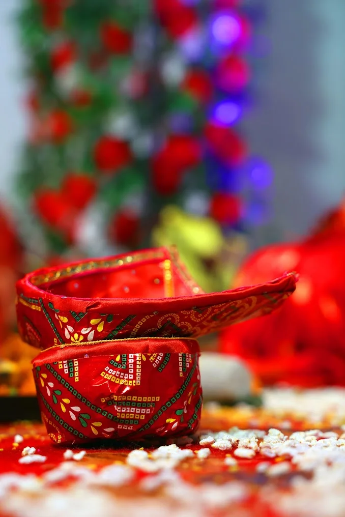 Red decorated ritual vessels arranged on rice with flowers and lights softly blurred behind